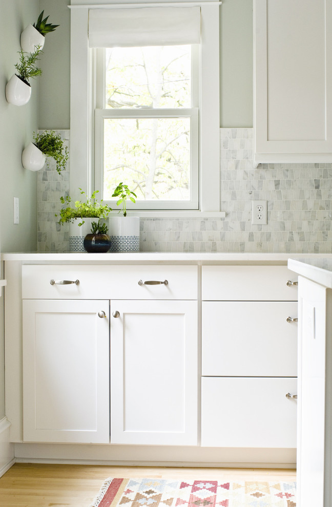 Inspiration for a transitional l-shaped eat-in kitchen remodel in Minneapolis with an undermount sink, flat-panel cabinets, white cabinets, solid surface countertops, gray backsplash, stone tile backsplash and stainless steel appliances