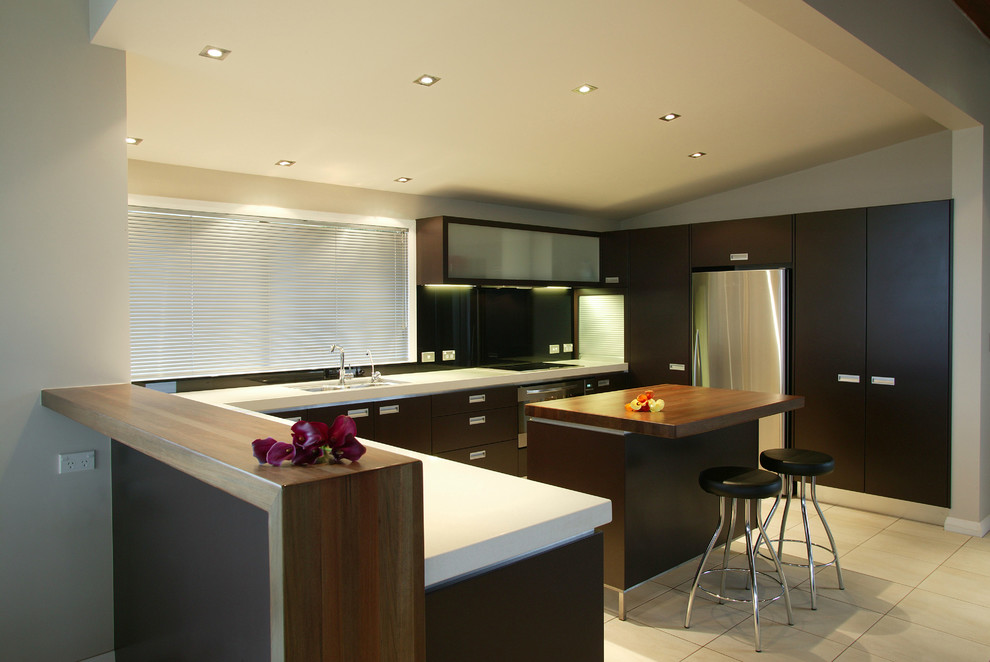 Example of a trendy l-shaped kitchen design in Los Angeles with stainless steel appliances, flat-panel cabinets, dark wood cabinets and wood countertops