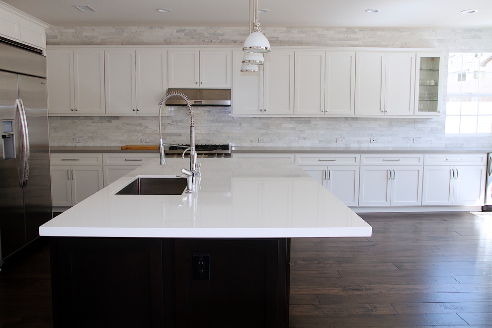 Example of a large trendy single-wall dark wood floor eat-in kitchen design in Los Angeles with white backsplash, marble backsplash, stainless steel appliances and an island