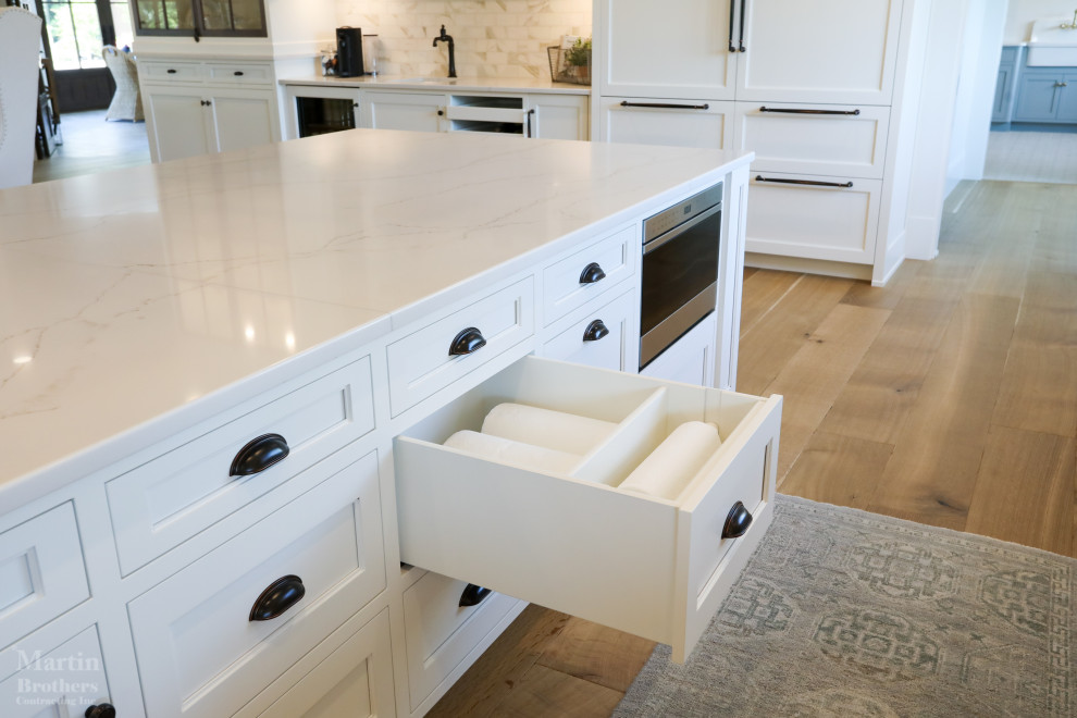 Inspiration for a large farmhouse l-shaped kitchen/diner in Other with a belfast sink, recessed-panel cabinets, white cabinets, engineered stone countertops, white splashback, marble splashback, integrated appliances, light hardwood flooring, an island, white worktops and a coffered ceiling.