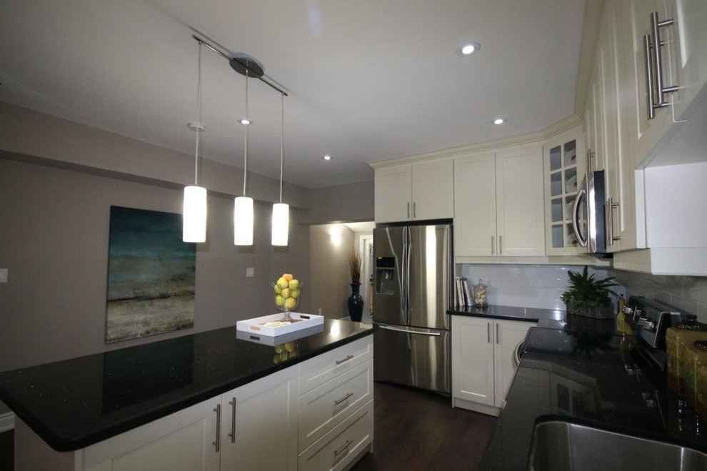 Photo of a medium sized contemporary grey and cream l-shaped kitchen/diner in Toronto with a double-bowl sink, recessed-panel cabinets, white cabinets, granite worktops, yellow splashback, ceramic splashback, white appliances, medium hardwood flooring and an island.