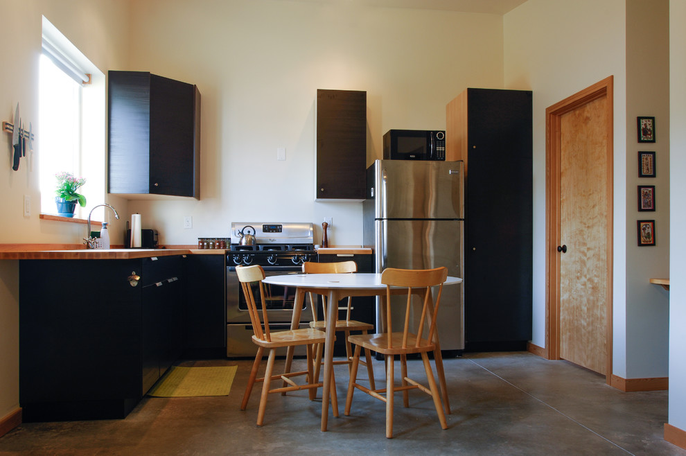 Modelo de cocinas en L actual pequeña abierta con fregadero encastrado, armarios con paneles lisos, puertas de armario negras, encimera de madera, electrodomésticos de acero inoxidable y suelo de cemento