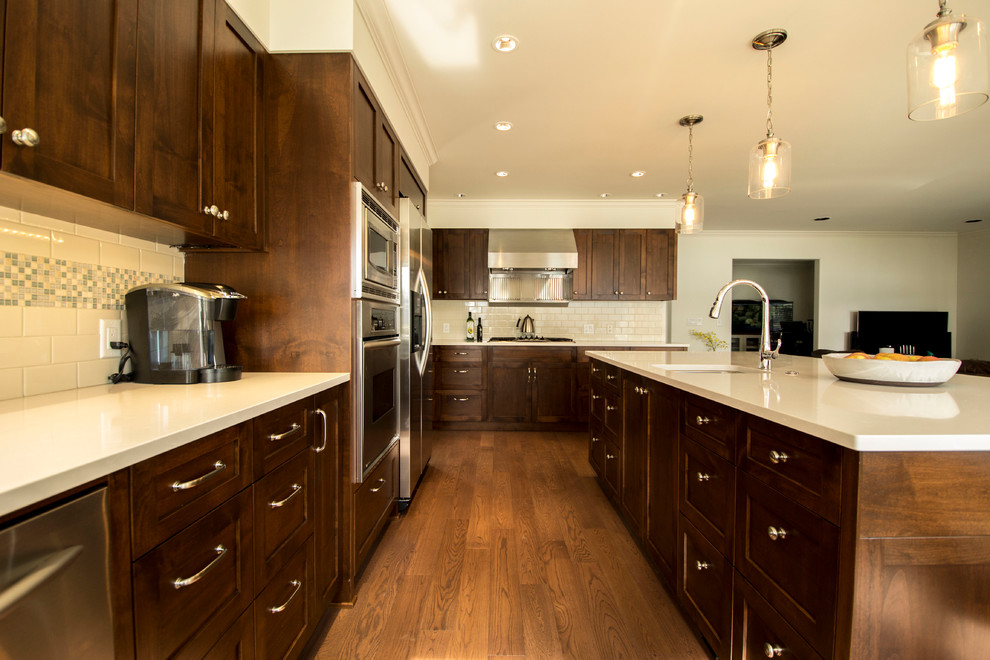 Large traditional l-shaped kitchen/diner in Vancouver with a submerged sink, shaker cabinets, medium wood cabinets, quartz worktops, white splashback, glass tiled splashback, stainless steel appliances, medium hardwood flooring and an island.