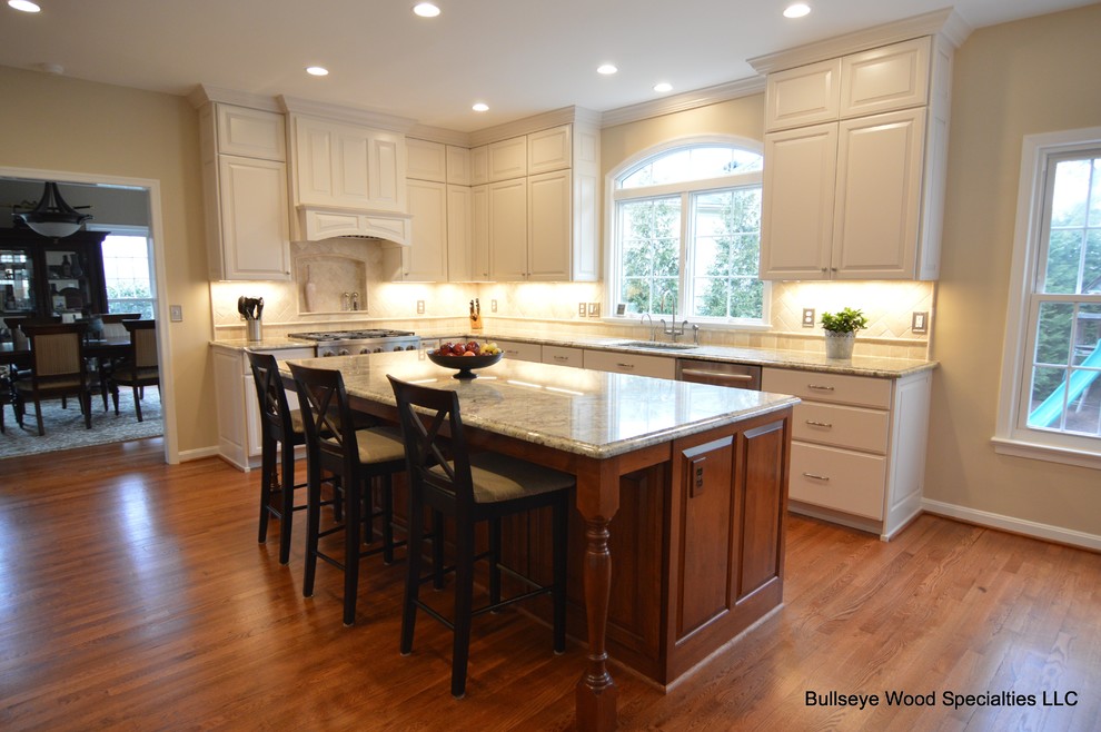 Large traditional l-shaped kitchen in DC Metro with a submerged sink, raised-panel cabinets, white cabinets, granite worktops, beige splashback, travertine splashback, stainless steel appliances, medium hardwood flooring, an island and brown floors.