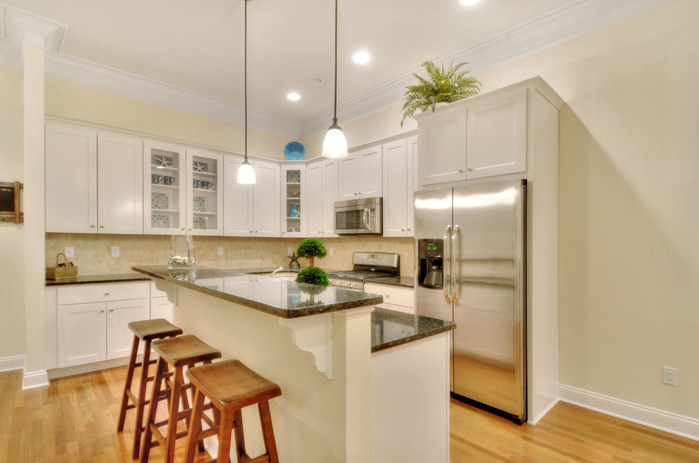 Inspiration for a transitional l-shaped light wood floor eat-in kitchen remodel in New York with an undermount sink, white cabinets, granite countertops, ceramic backsplash, stainless steel appliances and an island