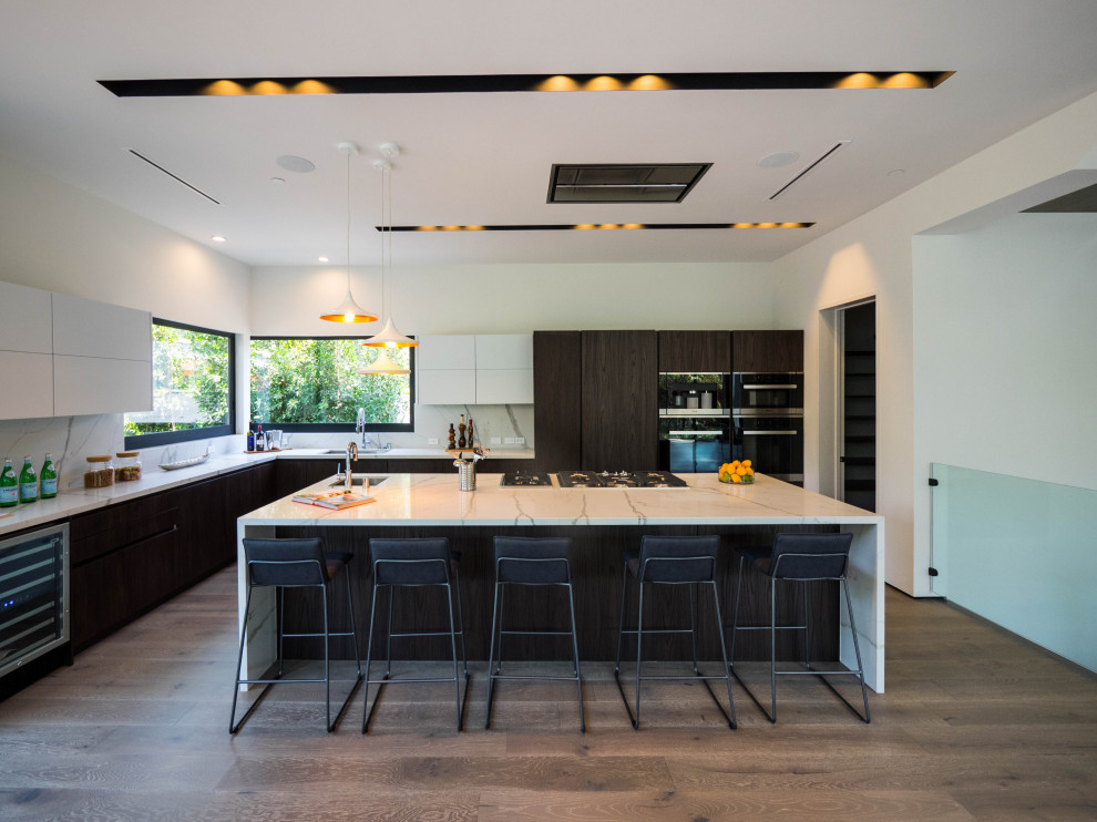 Inspiration for a large contemporary l-shaped kitchen/diner in Los Angeles with a submerged sink, flat-panel cabinets, dark wood cabinets, engineered stone countertops, white splashback, stone slab splashback, integrated appliances, an island, white worktops, medium hardwood flooring and brown floors.