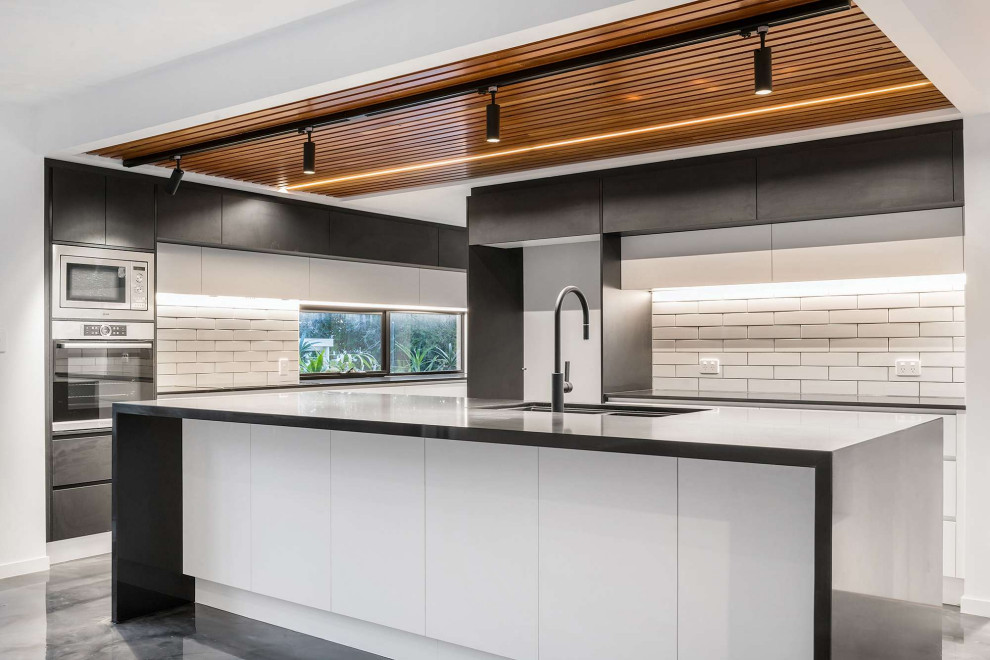 ゴールドコーストにある高級な広いコンテンポラリースタイルのおしゃれなキッチン (アンダーカウンターシンク、フラットパネル扉のキャビネット、白いキャビネット、クオーツストーンカウンター、白いキッチンパネル、サブウェイタイルのキッチンパネル、シルバーの調理設備、コンクリートの床、グレーの床、黒いキッチンカウンター、板張り天井) の写真
