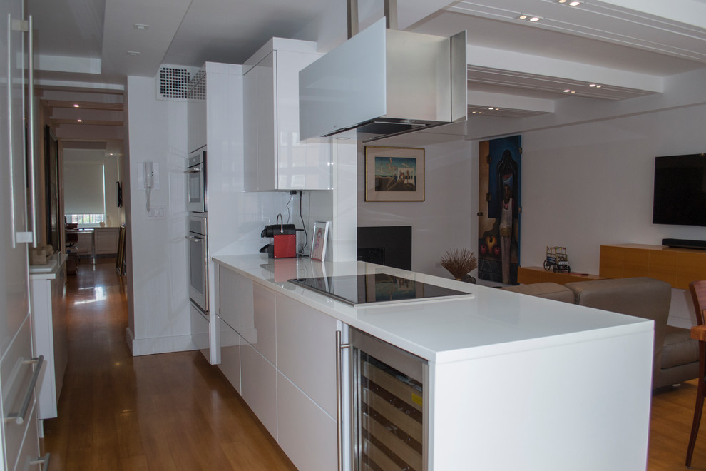 This is an example of a small modern galley kitchen in New York with flat-panel cabinets, white cabinets, stainless steel appliances and medium hardwood flooring.