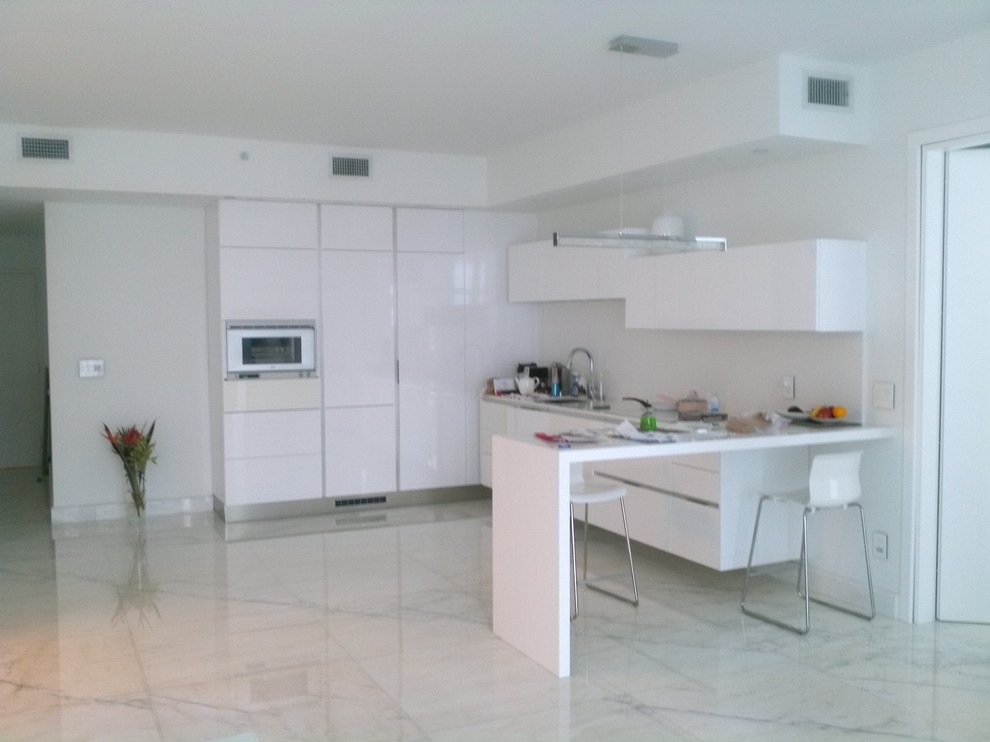 Photo of a small modern l-shaped open plan kitchen in Miami with a submerged sink, flat-panel cabinets, white cabinets, quartz worktops, white splashback, stone slab splashback, white appliances and marble flooring.