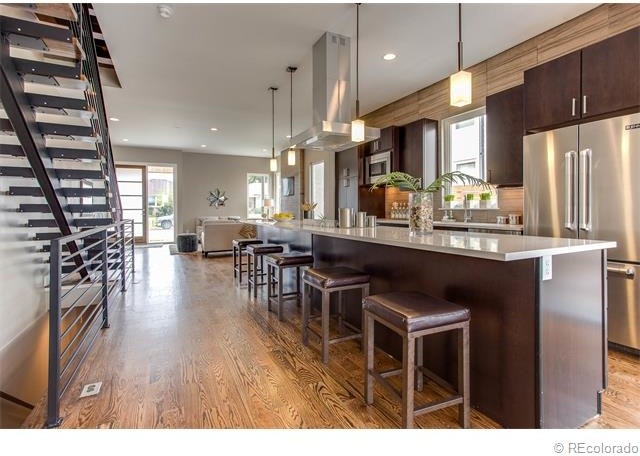 Open concept kitchen - large modern single-wall medium tone wood floor and brown floor open concept kitchen idea in Denver with flat-panel cabinets, dark wood cabinets, quartzite countertops, brown backsplash, wood backsplash, stainless steel appliances, an island and an undermount sink