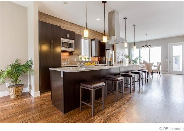 Large minimalist single-wall medium tone wood floor and brown floor open concept kitchen photo in Denver with flat-panel cabinets, dark wood cabinets, quartzite countertops, brown backsplash, wood backsplash, stainless steel appliances, an island and an undermount sink
