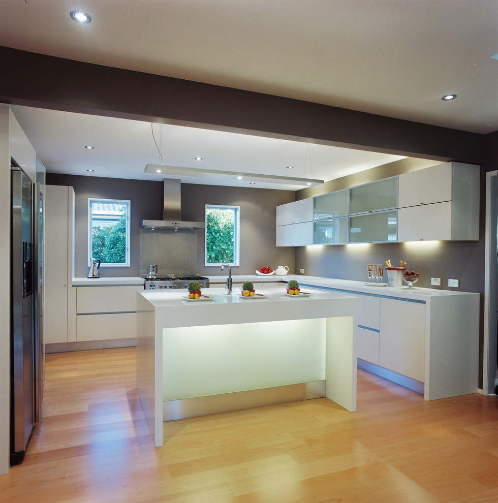 Diseño de cocina contemporánea con electrodomésticos de acero inoxidable, armarios con paneles lisos, puertas de armario blancas y salpicadero de vidrio templado
