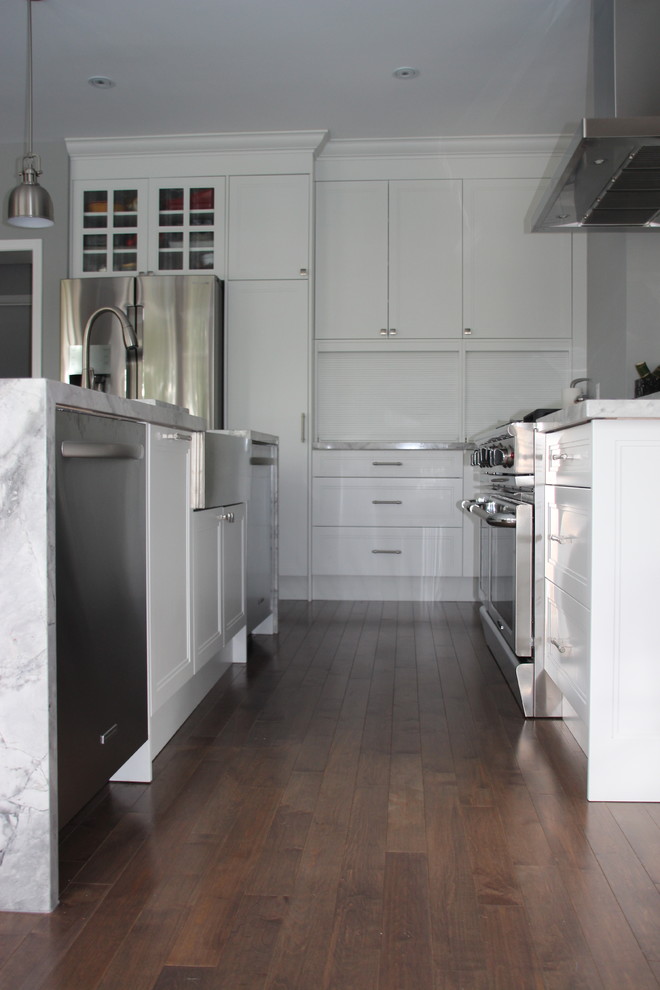 Inredning av ett modernt stort kök, med en rustik diskho, skåp i shakerstil, vita skåp, granitbänkskiva, rostfria vitvaror, mörkt trägolv och en köksö