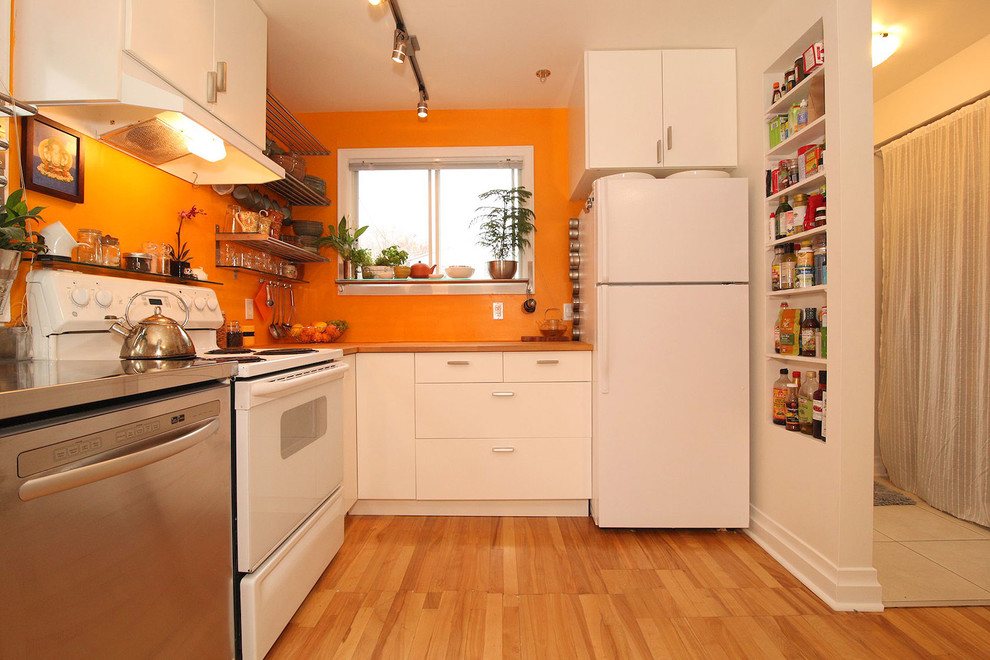Asiatisk inredning av ett litet kök, med en undermonterad diskho, släta luckor, vita skåp, bänkskiva i rostfritt stål, orange stänkskydd, rostfria vitvaror och ljust trägolv