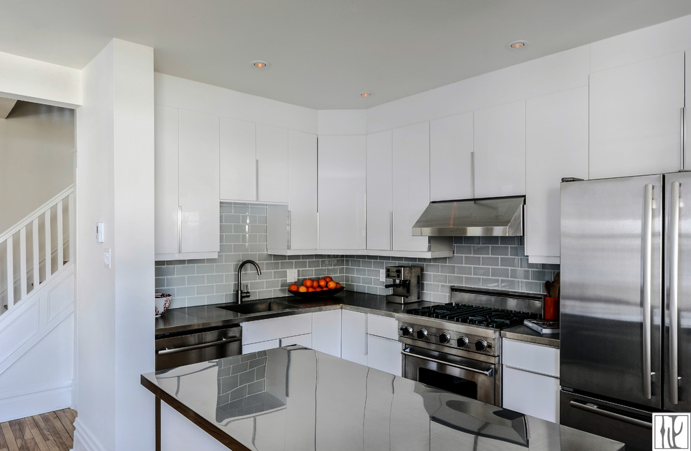 Eat-in kitchen - mid-sized contemporary l-shaped medium tone wood floor eat-in kitchen idea in Ottawa with an undermount sink, flat-panel cabinets, white cabinets, stainless steel countertops, gray backsplash, glass tile backsplash, stainless steel appliances and an island