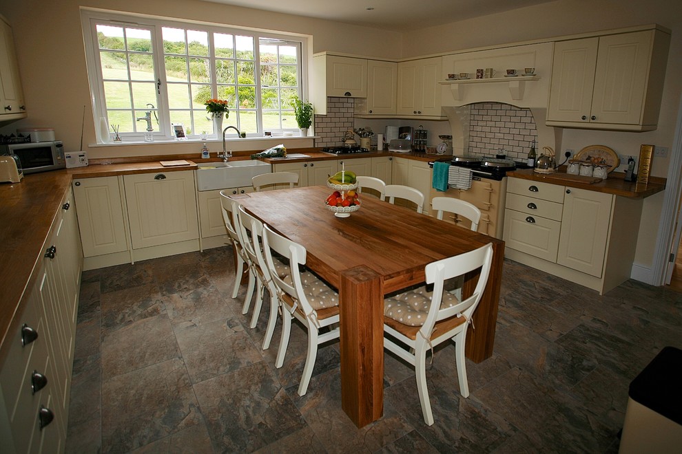 Große Landhaus Wohnküche in L-Form mit Doppelwaschbecken, Kassettenfronten, beigen Schränken, Arbeitsplatte aus Holz, Küchenrückwand in Weiß, Rückwand aus Keramikfliesen, Keramikboden, Kücheninsel und braunem Boden in Dorset