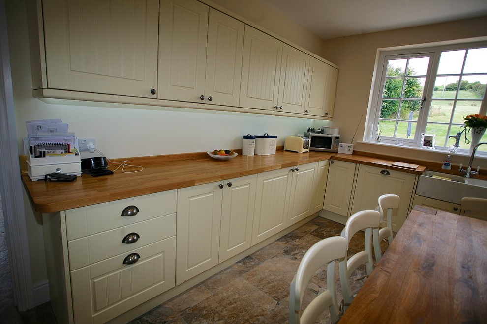 Eat-in kitchen - large farmhouse l-shaped ceramic tile and brown floor eat-in kitchen idea in Dorset with a double-bowl sink, beaded inset cabinets, beige cabinets, wood countertops, white backsplash, ceramic backsplash and an island