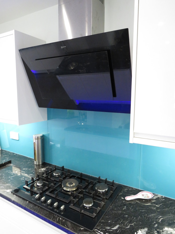 Bild på ett mellanstort funkis l-kök, med granitbänkskiva, en undermonterad diskho, släta luckor, vita skåp, blått stänkskydd, glaspanel som stänkskydd, integrerade vitvaror, klinkergolv i keramik, en köksö och grått golv