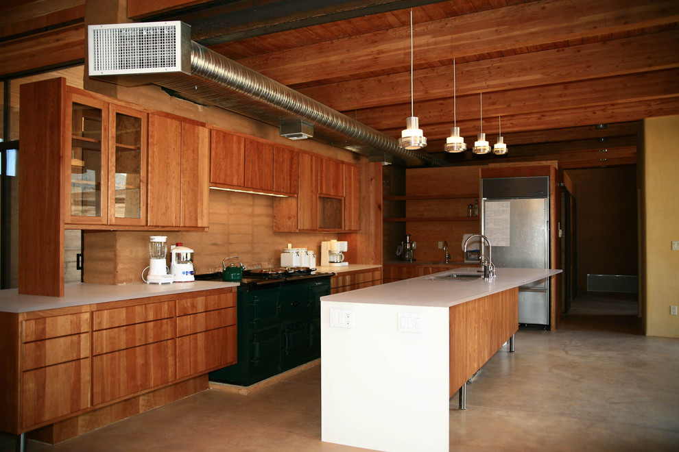 Aménagement d'une grande cuisine moderne en L et bois brun avec un placard à porte plane, un plan de travail en surface solide, un électroménager en acier inoxydable, sol en béton ciré, îlot et un sol marron.