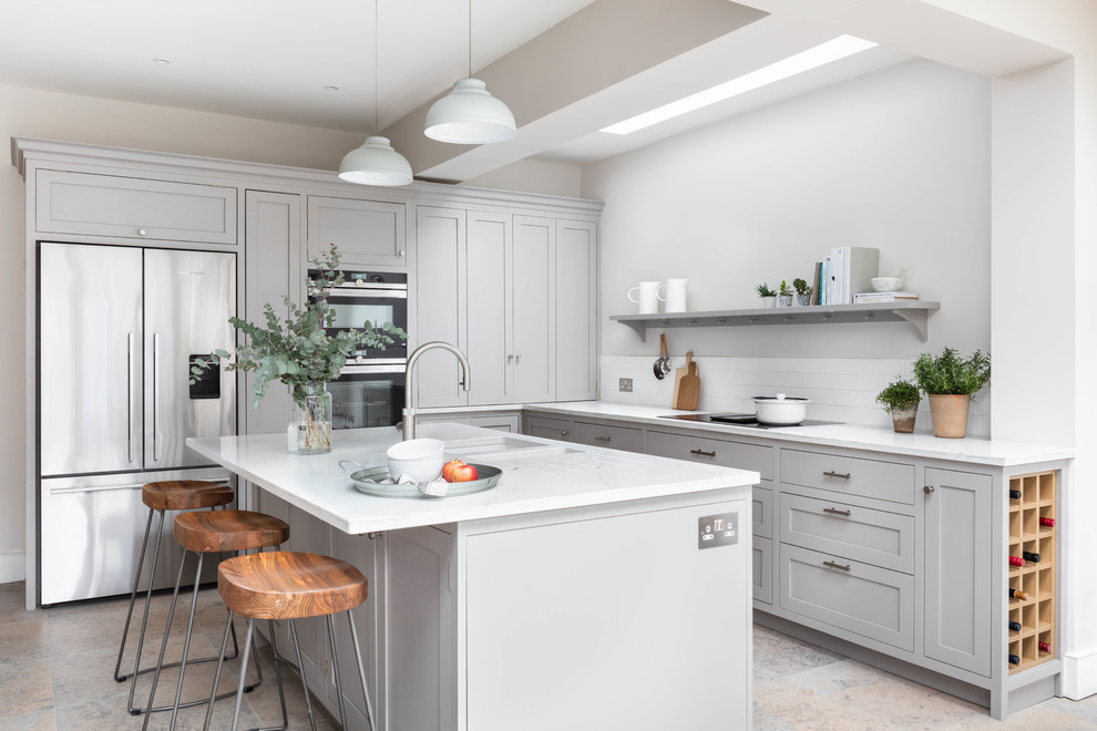 Photo of a traditional l-shaped kitchen in London with a submerged sink, shaker cabinets, grey cabinets, white splashback, stainless steel appliances, an island, grey floors and white worktops.
