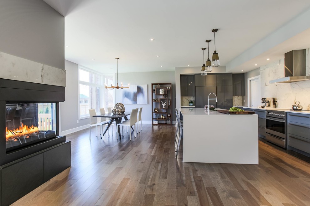 This is an example of a large modern galley open plan kitchen in Ottawa with a submerged sink, flat-panel cabinets, white cabinets, quartz worktops, white splashback, stone slab splashback, stainless steel appliances, light hardwood flooring, an island and beige floors.
