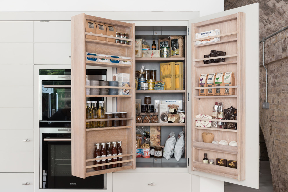 Cette image montre une arrière-cuisine design avec un placard à porte plane, des portes de placard blanches et un électroménager en acier inoxydable.