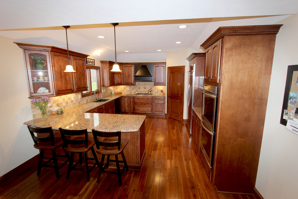 Eat-in kitchen - mid-sized traditional u-shaped medium tone wood floor eat-in kitchen idea in Cleveland with a double-bowl sink, raised-panel cabinets, medium tone wood cabinets, quartz countertops, beige backsplash, stainless steel appliances and an island