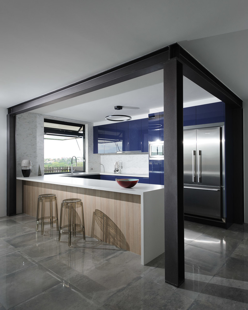 Foto di una cucina minimalista di medie dimensioni con lavello sottopiano, ante lisce, ante blu, paraspruzzi in marmo, elettrodomestici in acciaio inossidabile, pavimento in cemento e penisola