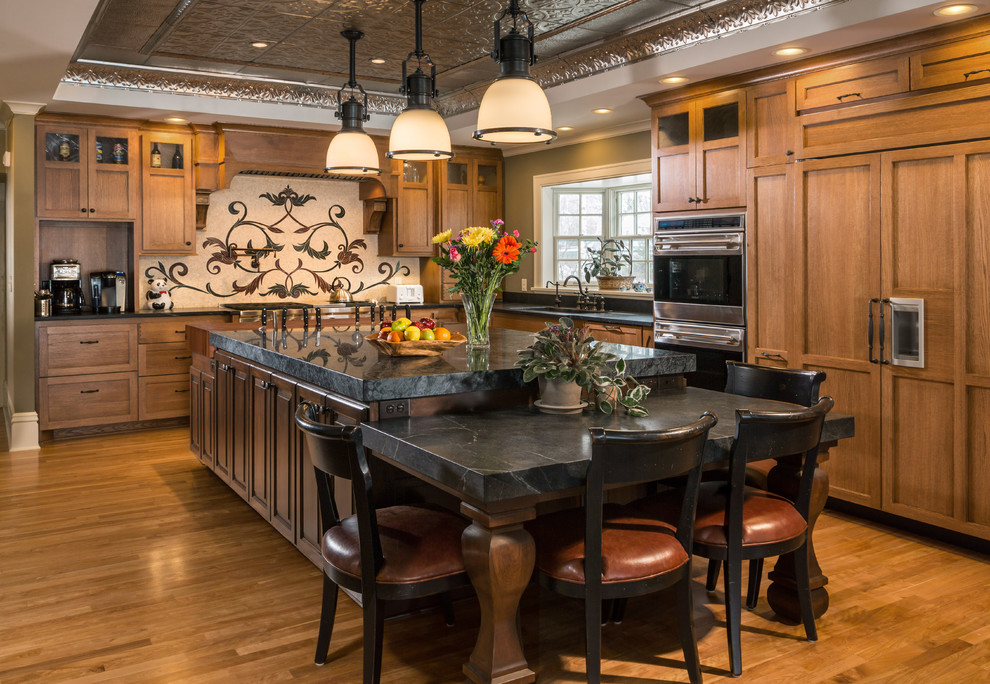 ミルウォーキーにあるトラディショナルスタイルのおしゃれなキッチン (ソープストーンカウンター、パネルと同色の調理設備、中間色木目調キャビネット、落し込みパネル扉のキャビネット) の写真