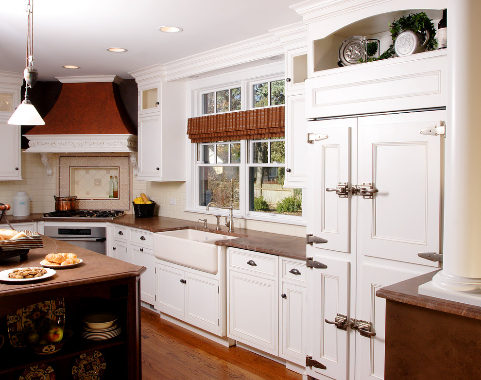 Exempel på ett stort klassiskt kök, med en rustik diskho, luckor med infälld panel, vita skåp, granitbänkskiva, vitt stänkskydd, stänkskydd i tunnelbanekakel, integrerade vitvaror, mellanmörkt trägolv och en köksö