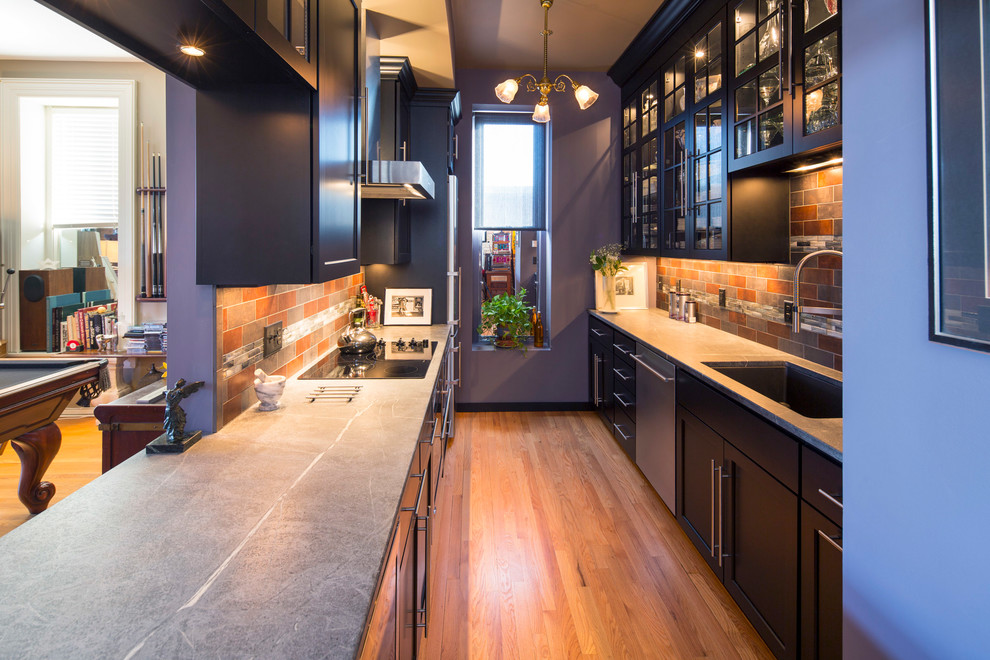 Inspiration for a small modern galley medium tone wood floor enclosed kitchen remodel in Minneapolis with an undermount sink, glass-front cabinets, black cabinets, soapstone countertops, porcelain backsplash, stainless steel appliances and a peninsula