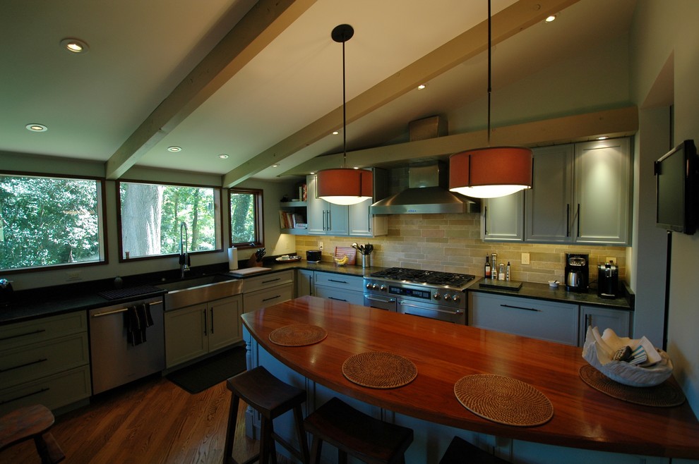 Inspiration for a mid-sized 1960s l-shaped medium tone wood floor kitchen remodel in DC Metro with a farmhouse sink, flat-panel cabinets, green cabinets, granite countertops, green backsplash, stone tile backsplash, stainless steel appliances and a peninsula
