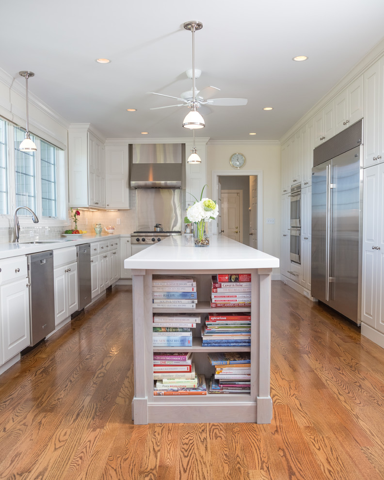 Example of a classic medium tone wood floor eat-in kitchen design in New York with white cabinets, marble countertops, white backsplash, ceramic backsplash, stainless steel appliances and an island