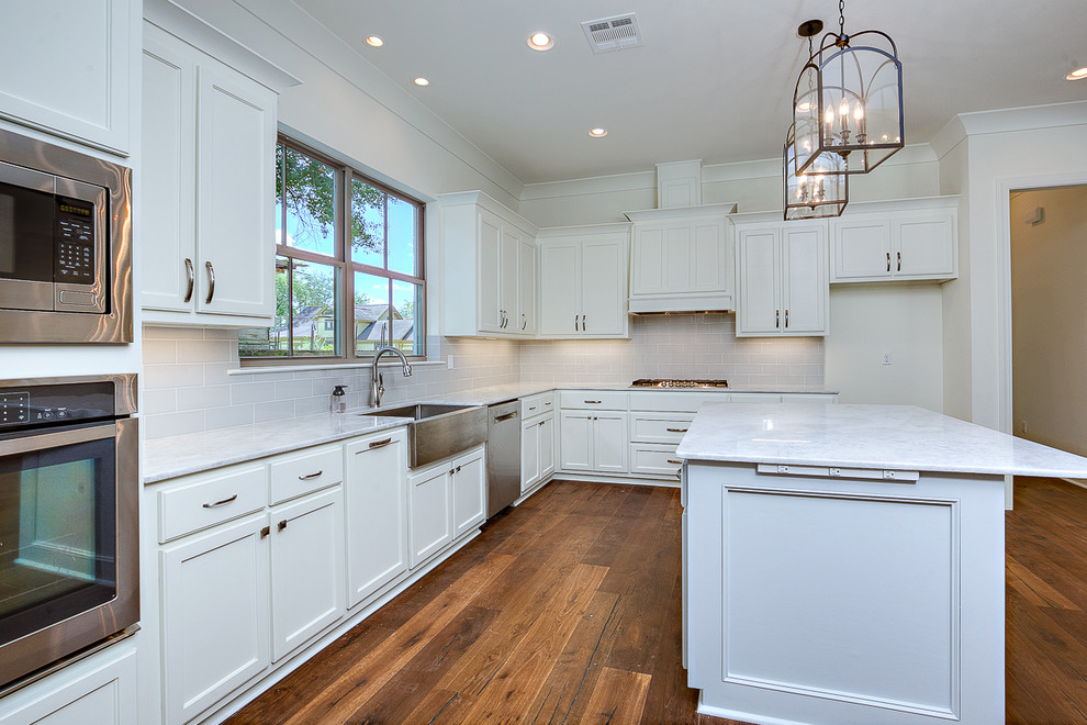 Medium sized farmhouse u-shaped open plan kitchen in New Orleans with a belfast sink, recessed-panel cabinets, white cabinets, marble worktops, grey splashback, porcelain splashback, stainless steel appliances, medium hardwood flooring, an island and brown floors.
