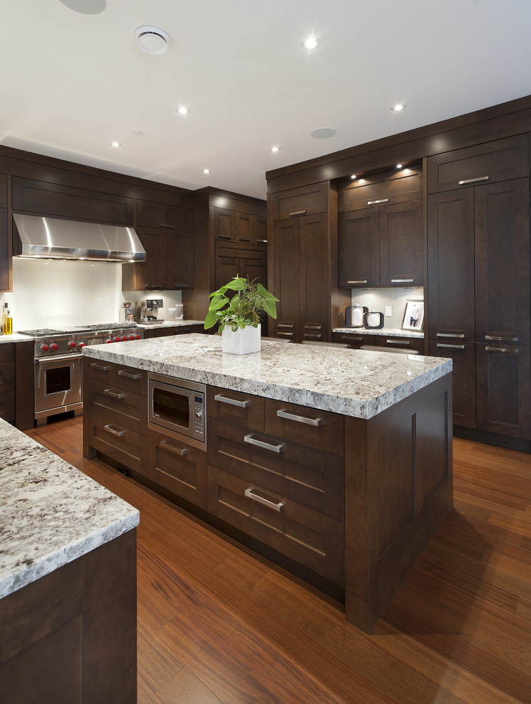 Klassische Küche in U-Form mit Küchengeräten aus Edelstahl, dunklen Holzschränken, Granit-Arbeitsplatte, Küchenrückwand in Weiß und weißer Arbeitsplatte in Vancouver