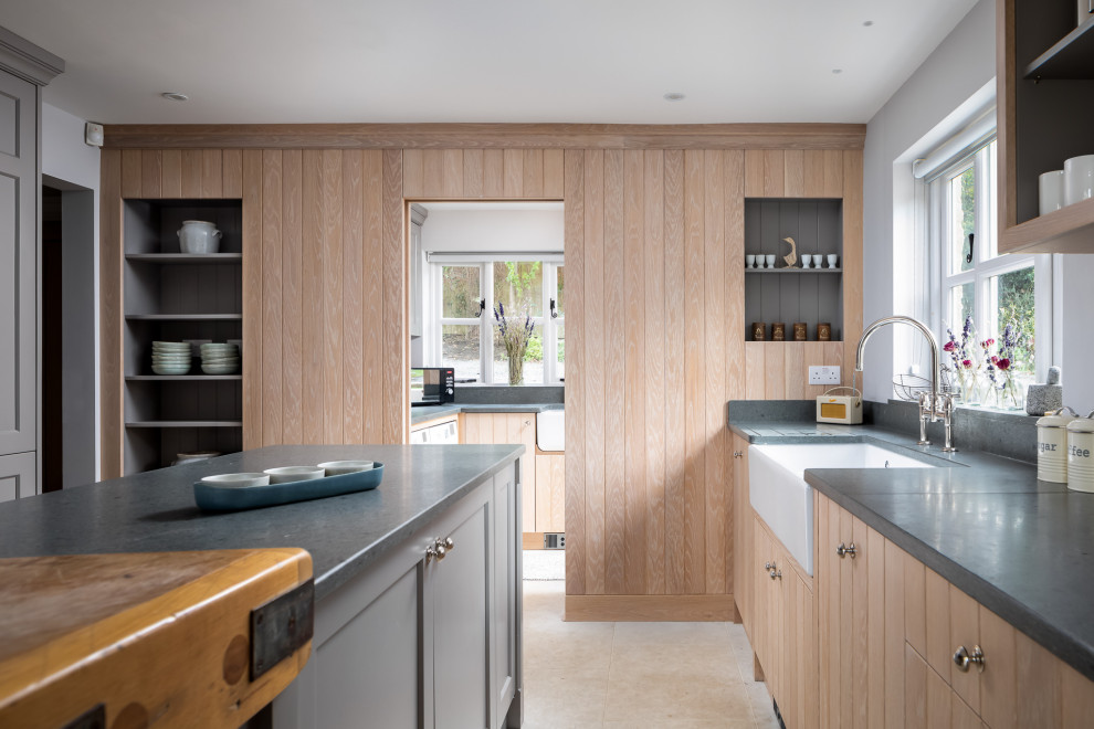 This is an example of a medium sized beach style galley enclosed kitchen in Gloucestershire with a belfast sink, shaker cabinets, medium wood cabinets, an island, beige floors and grey worktops.