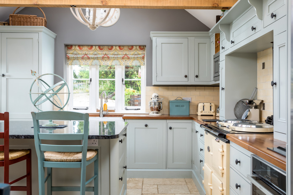 Große Country Wohnküche in L-Form mit blauen Schränken, Kücheninsel, beigem Boden, brauner Arbeitsplatte, Landhausspüle, Schrankfronten im Shaker-Stil, Arbeitsplatte aus Holz, Küchenrückwand in Beige, Rückwand aus Metrofliesen, bunten Elektrogeräten und gewölbter Decke in Gloucestershire