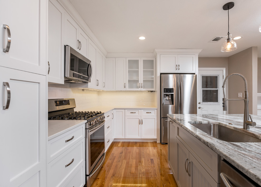 Exempel på ett mellanstort klassiskt kök, med en undermonterad diskho, skåp i shakerstil, vita skåp, granitbänkskiva, vitt stänkskydd, stänkskydd i tunnelbanekakel, rostfria vitvaror, mellanmörkt trägolv och en köksö