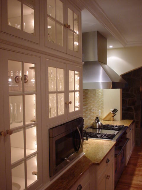 This is an example of a large traditional galley kitchen/diner in Newark with a belfast sink, beaded cabinets, white cabinets, granite worktops, multi-coloured splashback, glass tiled splashback, stainless steel appliances, light hardwood flooring, an island and beige floors.