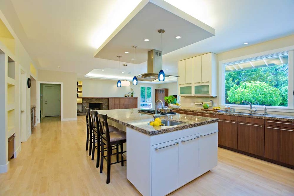 This is an example of a large contemporary u-shaped open plan kitchen in San Francisco with a submerged sink, flat-panel cabinets, granite worktops, white splashback, light hardwood flooring, white cabinets, stainless steel appliances, an island, beige floors and multicoloured worktops.