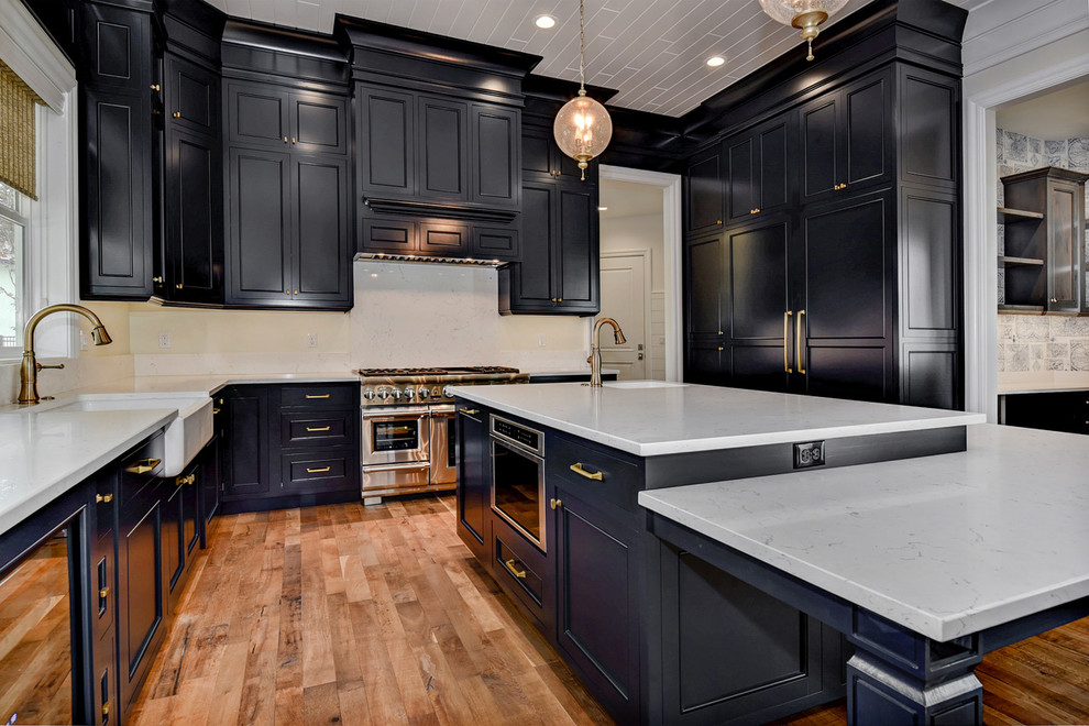 Large elegant l-shaped medium tone wood floor and multicolored floor eat-in kitchen photo in Boise with a farmhouse sink, raised-panel cabinets, blue cabinets, marble countertops, white backsplash, marble backsplash, stainless steel appliances and two islands