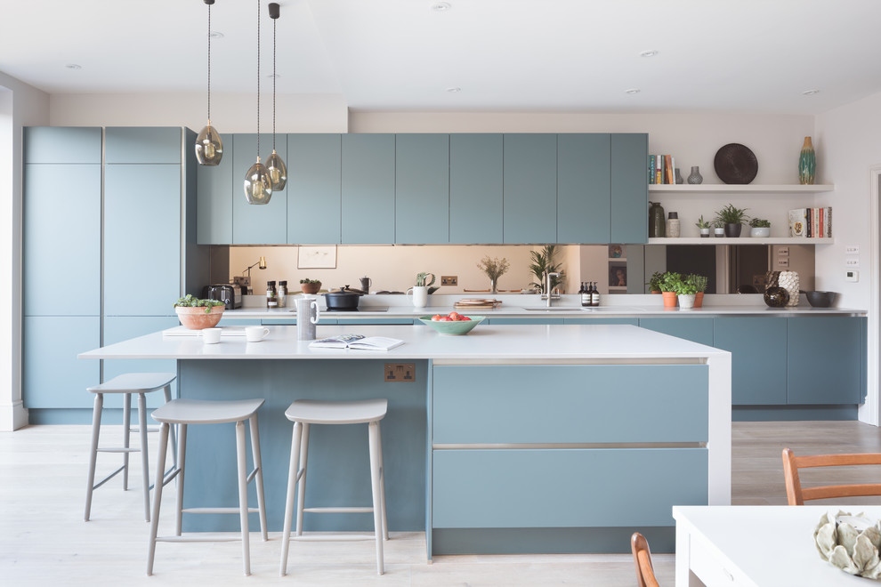 Design ideas for a medium sized contemporary single-wall kitchen/diner in London with a submerged sink, flat-panel cabinets, blue cabinets, an island, beige floors, mirror splashback and integrated appliances.