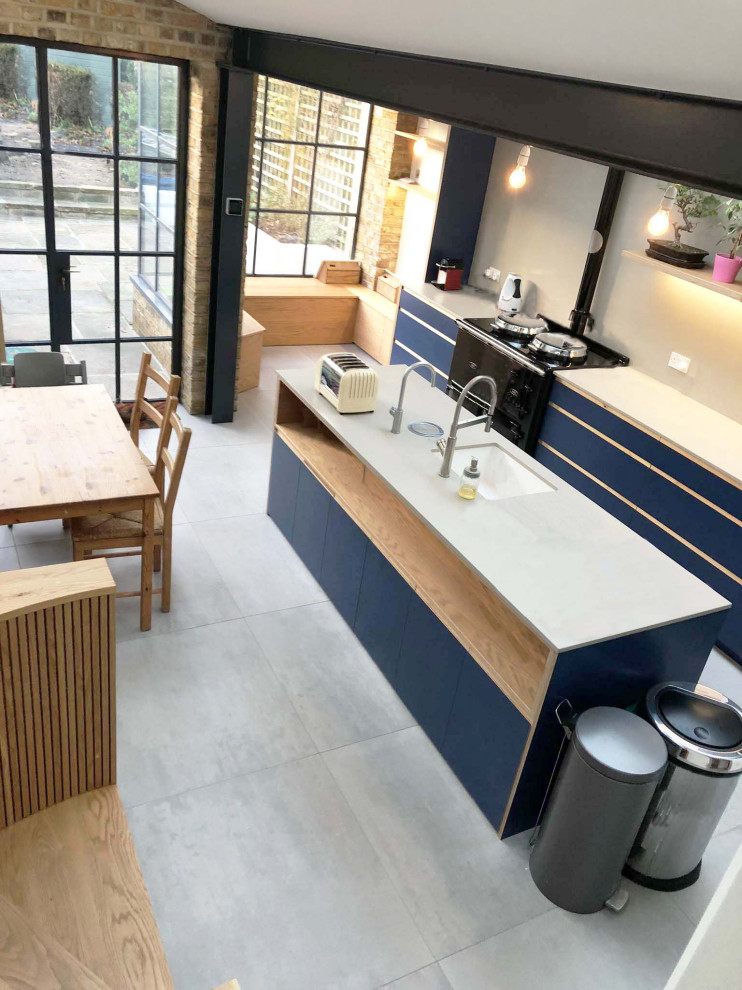 This is an example of a medium sized scandi single-wall kitchen/diner in London with a built-in sink, flat-panel cabinets, blue cabinets, engineered stone countertops, grey splashback, ceramic splashback, black appliances, ceramic flooring, an island, grey floors and grey worktops.