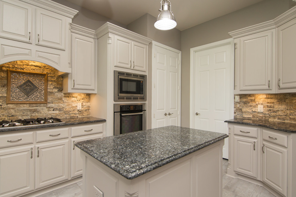 Mid-sized elegant u-shaped porcelain tile and gray floor eat-in kitchen photo in Dallas with an undermount sink, raised-panel cabinets, gray cabinets, granite countertops, beige backsplash, stone tile backsplash, stainless steel appliances, an island and blue countertops