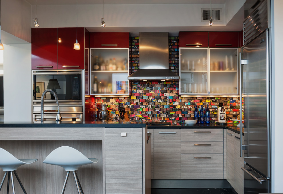 На фото: угловая кухня в современном стиле с обеденным столом, плоскими фасадами, красными фасадами, разноцветным фартуком, техникой из нержавеющей стали и островом