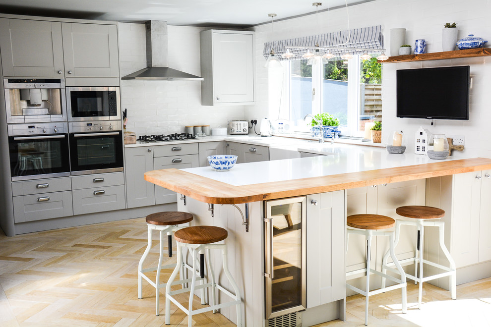 Landhaus Küche in U-Form mit Schrankfronten im Shaker-Stil, grauen Schränken, Küchenrückwand in Weiß, Rückwand aus Metrofliesen, Küchengeräten aus Edelstahl, hellem Holzboden und braunem Boden in Hampshire