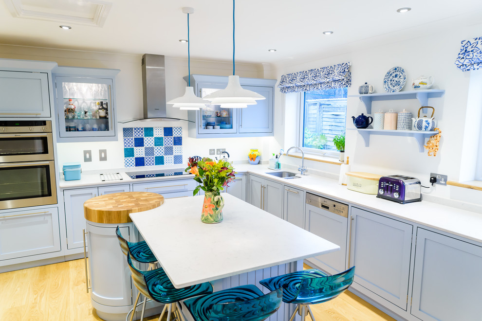 Design ideas for a medium sized beach style l-shaped kitchen in Other with a double-bowl sink, recessed-panel cabinets, blue cabinets, light hardwood flooring, an island, blue splashback and beige floors.