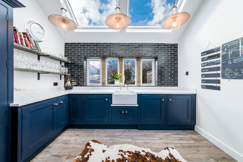 This is an example of a medium sized traditional l-shaped kitchen in Other with a belfast sink, blue cabinets, quartz worktops, black splashback, metro tiled splashback, light hardwood flooring, beige floors, white worktops and shaker cabinets.