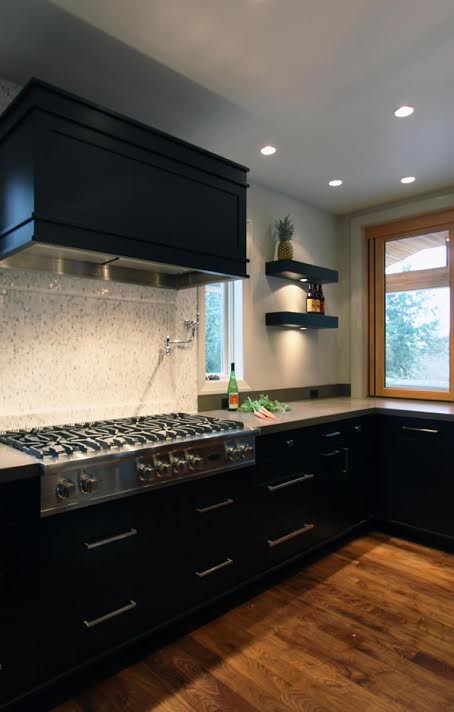 Foto på ett stort funkis kök, med vitt stänkskydd, rostfria vitvaror, en köksö, en undermonterad diskho, släta luckor, svarta skåp, marmorbänkskiva, stänkskydd i glaskakel, mellanmörkt trägolv och brunt golv