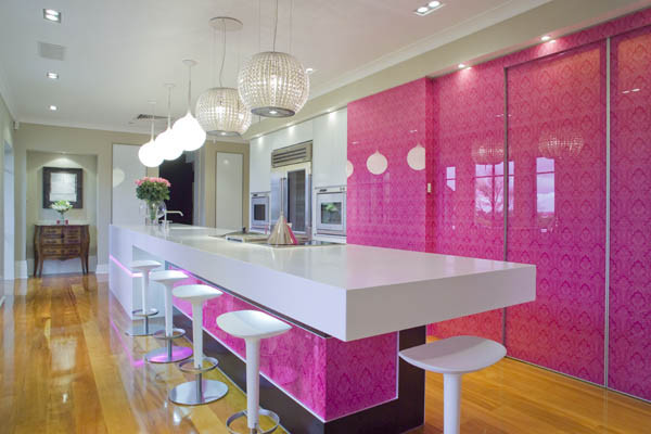 Diseño de cocina minimalista grande con armarios con paneles lisos, encimera de cuarzo compacto, salpicadero rosa, salpicadero de vidrio templado, electrodomésticos de acero inoxidable, suelo de madera clara y una isla